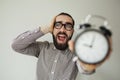 Man in panic holds alarm clock and head in fear of deadline