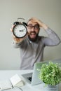 Man in panic holds alarm clock and head scared of deadline