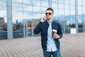 A man with a paper Cup of coffee, goes through the city, a handsome guy in stylish clothes and sunglasses, making a phone call Royalty Free Stock Photo