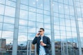 A man with a paper Cup of coffee, goes through the city, a handsome guy in stylish clothes and sunglasses, making a phone call Royalty Free Stock Photo