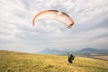 A man paraglider taking off from the edge of the mountain with fields in the background. Paragliding sports