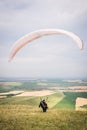 A man paraglider taking off from the edge of the mountain with fields in the background. Paragliding sports