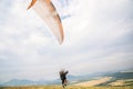 A man paraglider taking off from the edge of the mountain with fields in the background. Paragliding sports