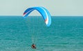Man paragliding with blue parachute above water sea, clear sky