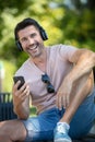 man on park bench using smartphone and wearing headphones Royalty Free Stock Photo