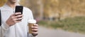 A man in the park drinking coffee and holding a phone in his hand