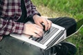 Man in the park sitting on the grass with a laptop, close-up hands and laptop. Royalty Free Stock Photo