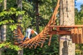 Man passes through hanging ladder attraction in rope adventure park in summer forest of Caucasus Mountains