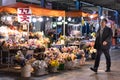 Man passing by a flowers stall at night. Street market. Man coming back home from work or a dinner with colleagues / friends.