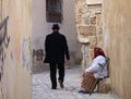 Man passing a narrow street around an old lady sitting