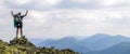 Man on peak of mountain. Emotional scene. Young man with backpack standing with raised hands on top of a mountain and enjoying mo