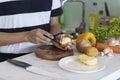 Man peeling and cutting a potato on a white kitchen table with vegetables in the background Royalty Free Stock Photo