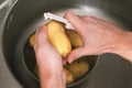 A man peels potatoes with a vegetable peeler in the sink. Preparation of potatoes for cooking. Cleaning peel from