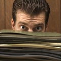 Man peering from behind pile of folders.