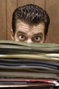 Man peering from behind pile of folders.