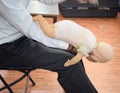 Man performing CPR on baby training doll dummy with one hand compression. First Aid Training - Cardiopulmonary resuscitation.