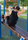 A man performs an exercise lifting the case on an inclined bench on the street on a sports ground