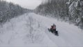 Man performs a jump on a snowmobile on a winter road along snow covered forest. Clip. Winter sport and leisure concept.