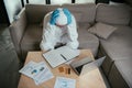 Man in personal protective equipment touching head near laptop, blank notebook