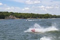 Man on Personal Water Craft landing in a spray of water after jumping a wake at the lake with speedboat and houses and boat docks Royalty Free Stock Photo