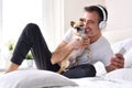 Man petting his chihuahua dog listening to music on bed