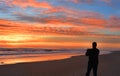 Man with phone on the beach at sunrise.