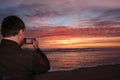 Man with phone on the beach at sunrise.