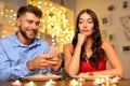 Man on phone smiling, woman bored at candlelit dinner