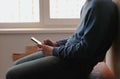 Man with phone. Unrecognizable young man browsing internet pages in mobile phone sitting on balcony near the window.