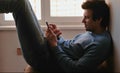 Man with phone. Young man chatting in mobile phone sitting on balcony near the window.