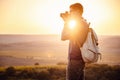 Man photographer with backpack and camera taking photo of sunset mountains