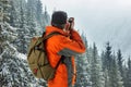 A man photographes a winter landscape. Against the background of mountains and pines