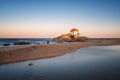Man photographing beautiful chapel Capela do Senhor da Pedra on the beach at sunset in Miramar, in Portugal