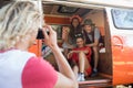 Man photographing smiling friends sitting in camper van