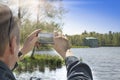 The man photographs on the cell phone on the bank of the lake the pavilion