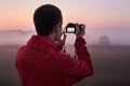 A man photographs a dense fog on an early morning at dawn