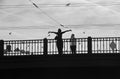 A man photographs a woman with her hands up on the bridge. Over a woman flying birds