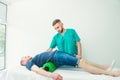 Man at the physiotherapy doing physical exercises with his therapist, they using a massage roll. A chiropractor treats patient`s