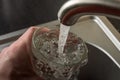 A man picks up drinking water in a glass from under the kitchen faucet