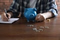 Man with piggy bank counting money at table, focus on scattered coins Royalty Free Stock Photo