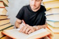 A man between piles of books wallowed in work - outlines and writes out information in a notebook