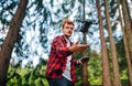 Man pilot in a red shirt stands in the woods and catches the drone with his hand after the flight, focus on the drone Royalty Free Stock Photo