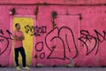 man in a pink sweater and yellow sneakers, against a background of a house with a wall in the color of the sweater Royalty Free Stock Photo