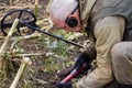 A man with a pinpointer in his hand is looking for a find in the ground. Next to it is a metal detector. On the