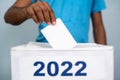 Man placing ballot paper into 2022 ballot box - concept of 2022 election. voting and democracy