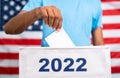 Man placing ballot paper into 2022 ballot box in front of american flag - concept of 2022 midterm US election, voting
