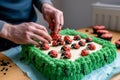 man placing fondant ladybugs on cake with green icing hedges