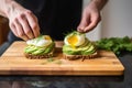 man placing poached egg on top of sliced avocado toast