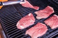 Man placing raw meat on to a hot barbecue to grill using a pair of wooden tongs, close up view over a dark background Royalty Free Stock Photo