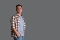 A man in a plaid shirt and a gray T-shirt stands on a gray background with his hands in his pockets, copyspace Royalty Free Stock Photo